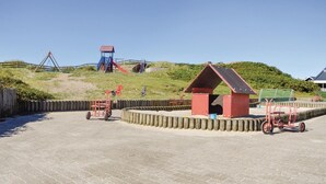 Un parque infantil con tobogán, columpios y un pequeño edificio rojo.