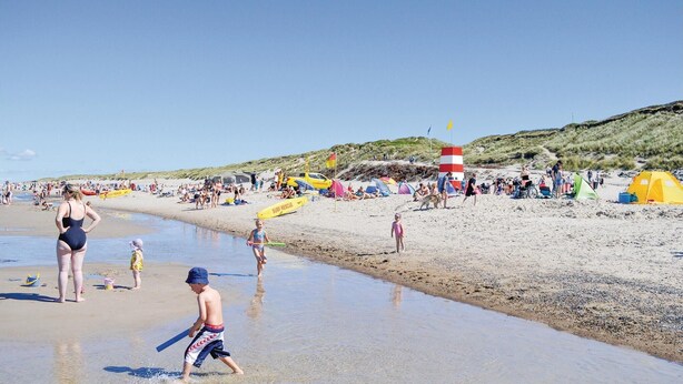 Escena de playa con gente, tiendas de campaña y una torre de salvavidas.