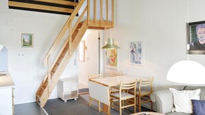 Una habitación moderna con una escalera de madera, un comedor con mesa y sillas, un sofá y un televisor montado en la pared.