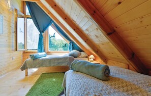 Cozy attic bedroom with two single beds, a bedside table, and a window with curtains.