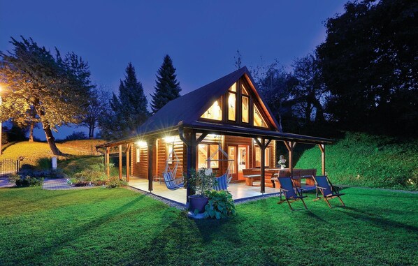 Cozy cabin with a gabled roof and covered porch, set amidst well-maintained grass and trees.