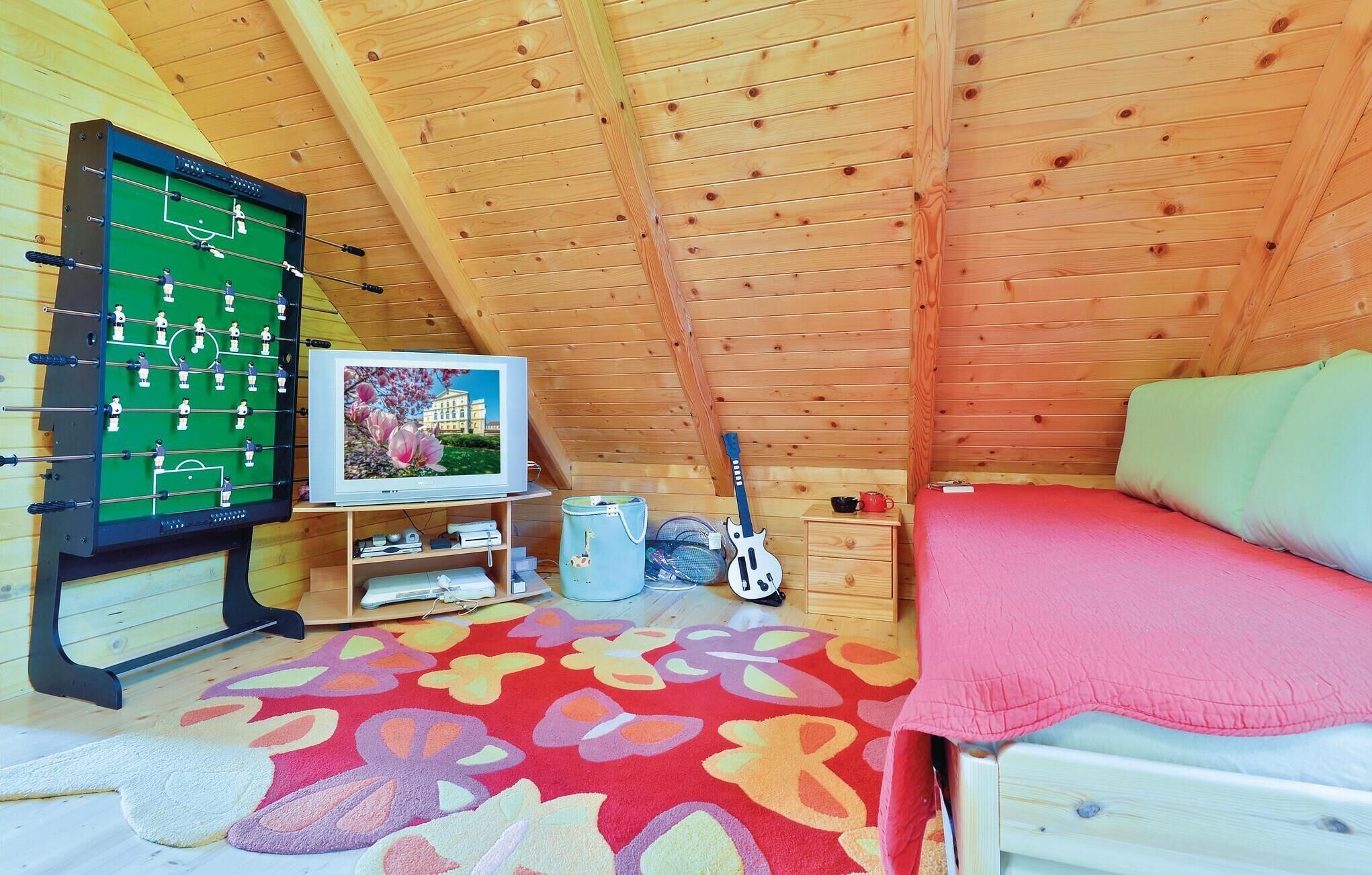 A cozy attic room with a foosball table, a television, a guitar, and a bed with a red blanket.