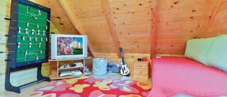A cozy attic room with a foosball table, a television, a guitar, and a bed with a red blanket.