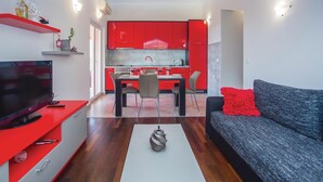 A modern living room with a flat-screen TV, a grey sofa with a red pillow, and a dining area with a red kitchen in the background. - 1 bedroom gorgeous apartment in Makarska (Makarska)