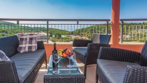 A balcony with wicker furniture, a glass table with a bottle and fruit, and a view of a green landscape. - 1 bedroom gorgeous apartment in Makarska (Makarska)