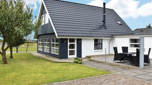 A modern house with a dark roof, large windows, and a patio area with outdoor furniture. - Cozy home in Lemvig with WiFi (Lemvig)
