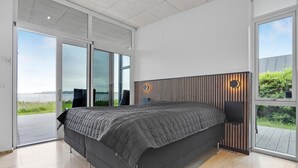 A modern bedroom with a large bed, sliding glass doors leading to a balcony, and a view of the outdoors.