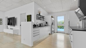 A modern kitchen with white cabinetry, a built-in oven, a coffee maker, and a large window offering a view of greenery.