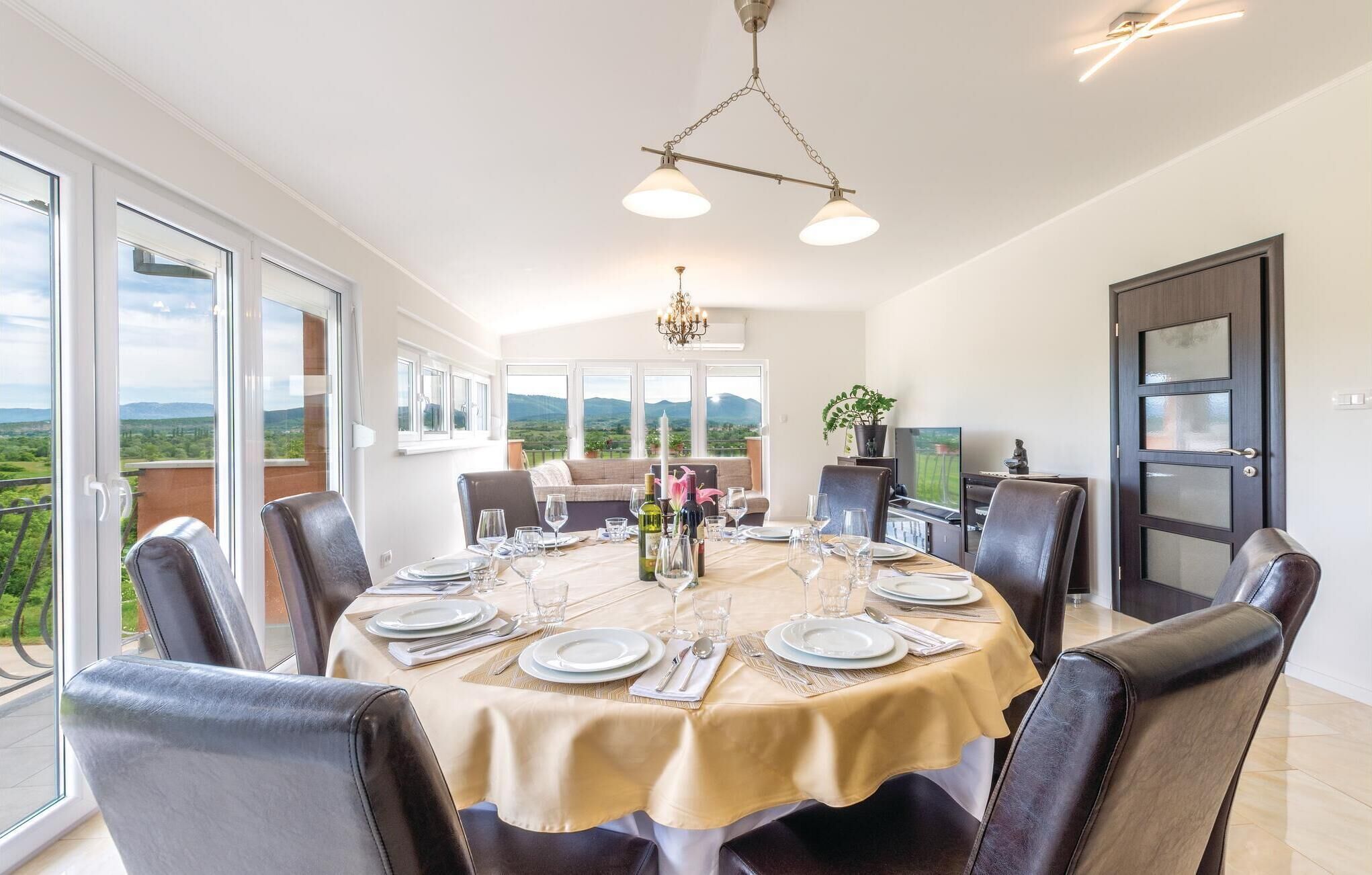 A dining area with a table set for six, large windows, and a view of the countryside.