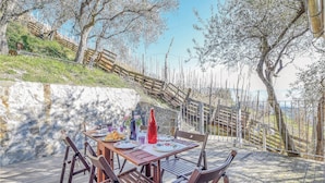 Una terraza de madera con una mesa para dos, rodeada de sillas, con vistas a una zona costera con árboles y una valla.