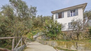 Un sendero de piedra que lleva a un edificio blanco con persianas, rodeado de olivos y un muro de piedra.