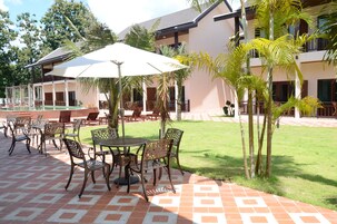 Un patio con mobiliario exterior, piscina y un edificio de varios pisos.