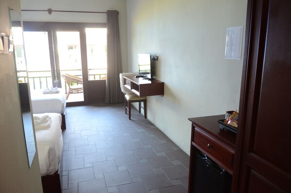 A hotel room with a bed, a desk, a chair, and a small cabinet. There is a balcony with a view outside.