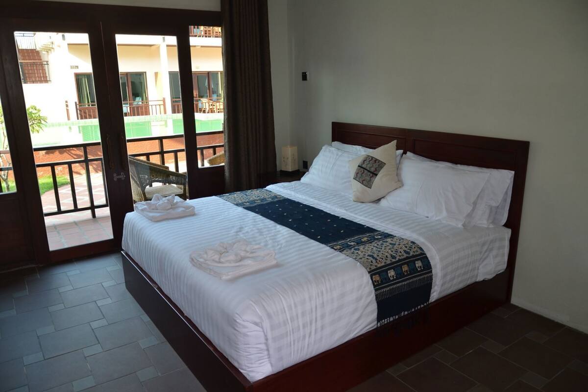 Una camera d'albergo con un letto, vista attraverso una porta in vetro e un balcone.