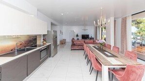 Cozinha moderna com ilha central, área de refeições com cadeiras cor-de-rosa e vista para uma piscina.