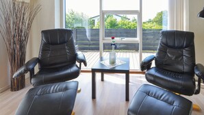 A modern living room with two black leather chairs facing a glass table. A large window offers a view of a wooden deck and greenery outside. - 3 bedroom nice home in Vestervig (Vestervig)