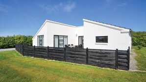 A modern white building with a sloped roof, a wooden fence, and a grassy area in front. - 3 bedroom nice home in Vestervig (Vestervig)