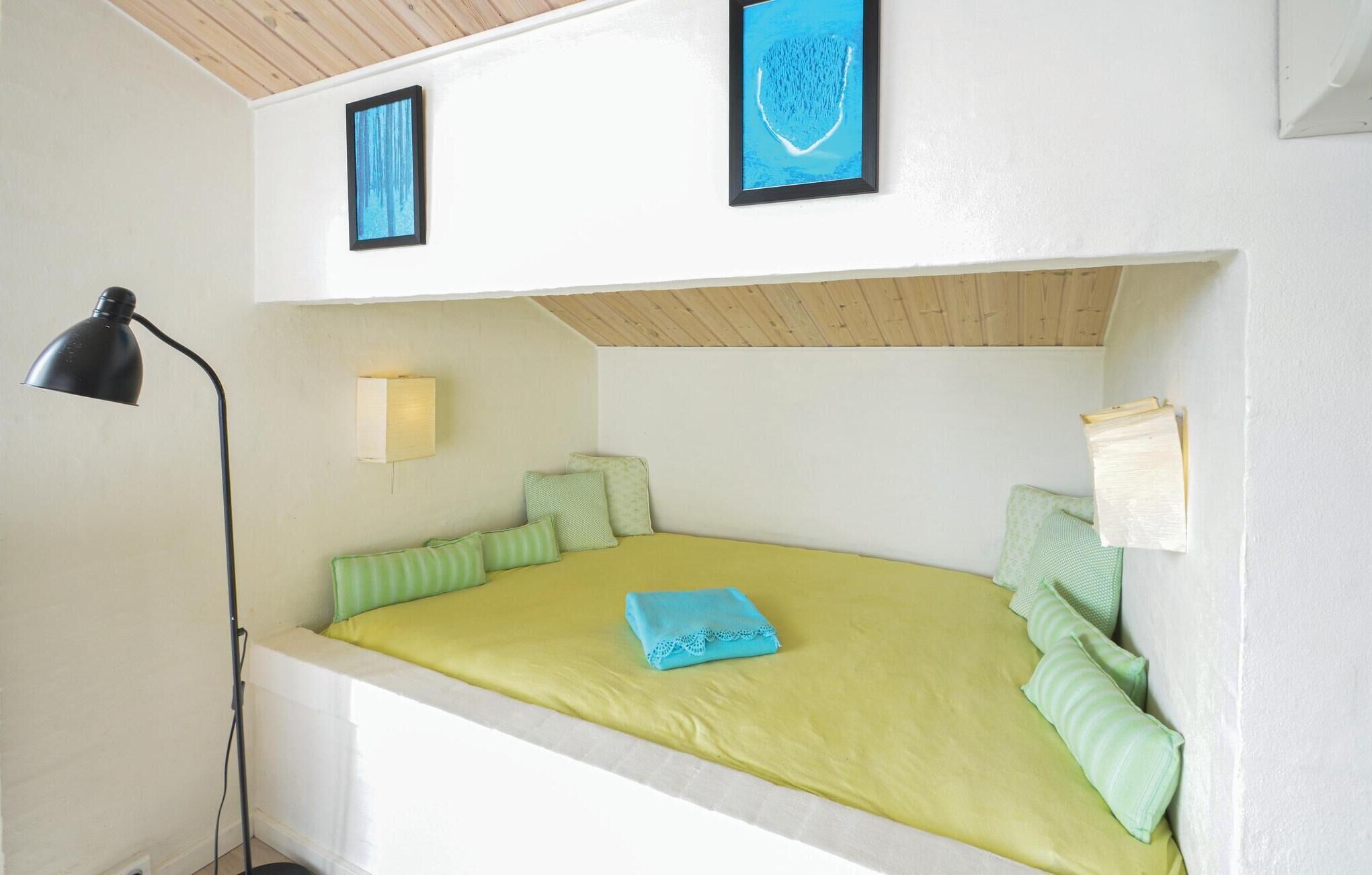 Ein kleines Zimmer mit einem Einzelbett, schrägem Giebeldach, einer Schreibtischlampe, einer Wandleuchte und zwei gerahmten Bildern.