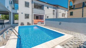 Ein Pool mit Metallleiter, umgeben von einer gepflasterten Liegefläche mit Liegestühlen.