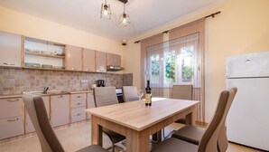 A modern kitchen with a dining area, featuring a wooden table and chairs, a refrigerator, and a window with curtains. - Beautiful home in Sukosan (Sukosan)