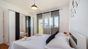 A hotel room with a large bed, a mirror, a window with curtains, and a hanging light fixture. - Beautiful home in Sukosan (Sukosan)
