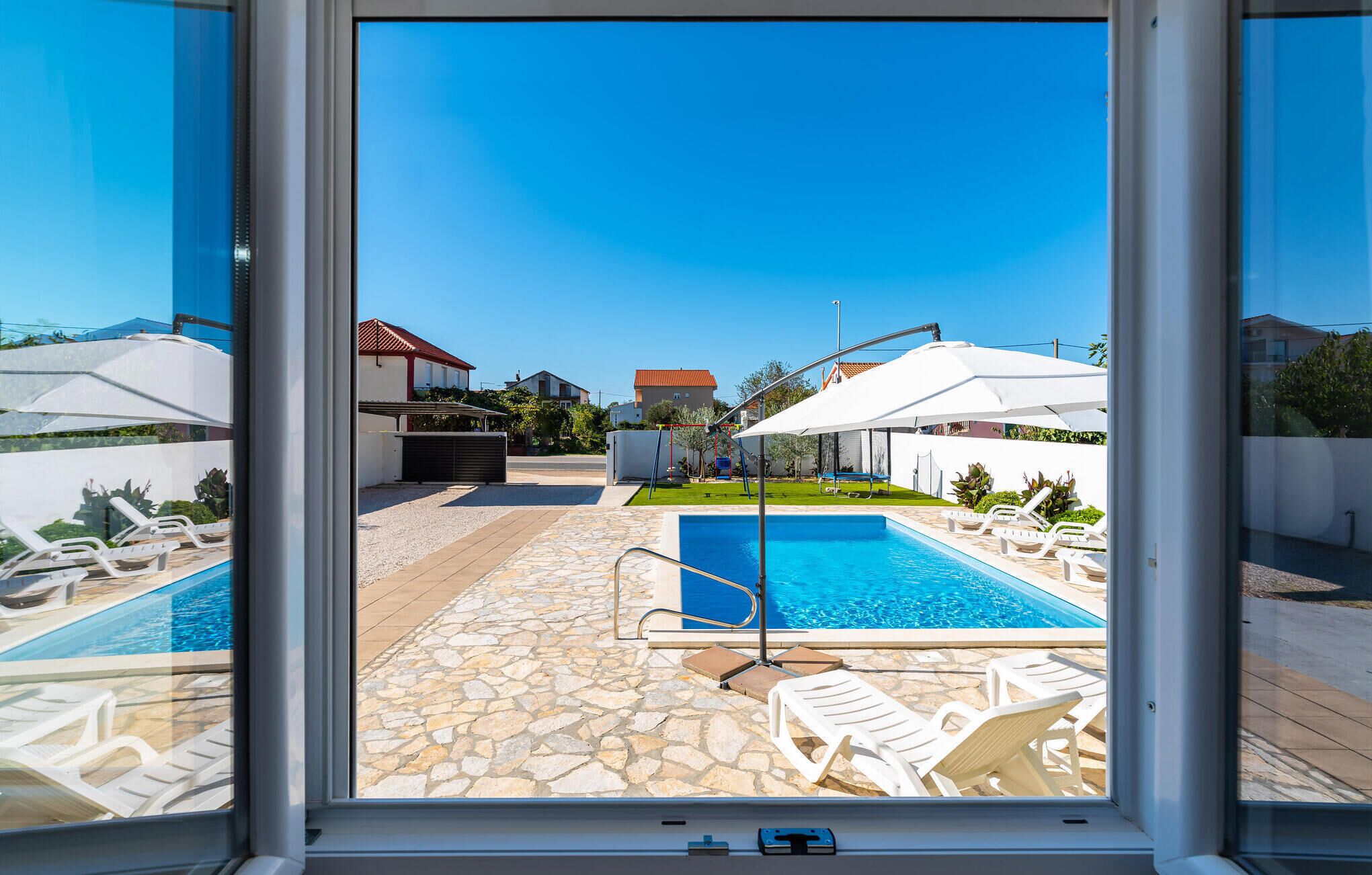 Uma área de piscina com piso de pedra, cadeiras de lounge brancas e guarda-sóis.