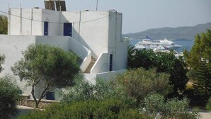 A modern building with a staircase leading to a door, surrounded by greenery, with a cruise ship visible in the background. - Kapetan Giannis (Milos)