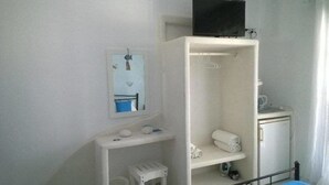 A small, white room with a bed, a bedside table, a TV, and a small cabinet. - Kapetan Giannis (Milos)