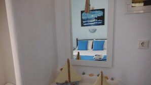 A bathroom with a white sink, two decorative sailboats, a mirror reflecting a bed with blue pillows, and a small shelf with seashells. - Kapetan Giannis (Milos)