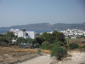 Un pueblo costero con edificios blancos, un camino de tierra y una vista despejada del mar y colinas distantes.