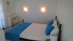 Una cama con colcha azul y blanca, dos luces empotradas en la pared y una mesita de noche blanca con una lámpara.