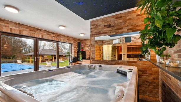A modern spa room with a hot tub, brick walls, and a large window overlooking a garden.
