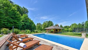 A swimming pool with lounge chairs and a gazebo in a garden setting.