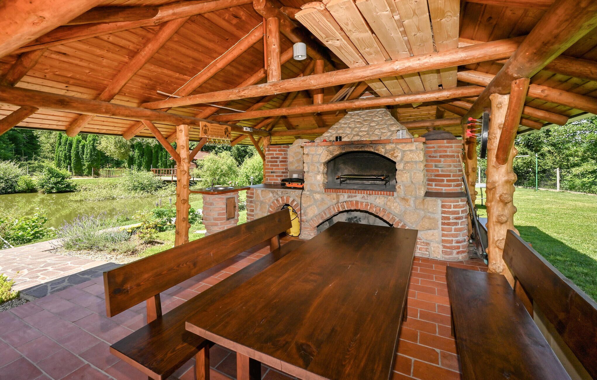 Un pabellón de madera al aire libre con un horno de pizza de ladrillo y una mesa de picnic.