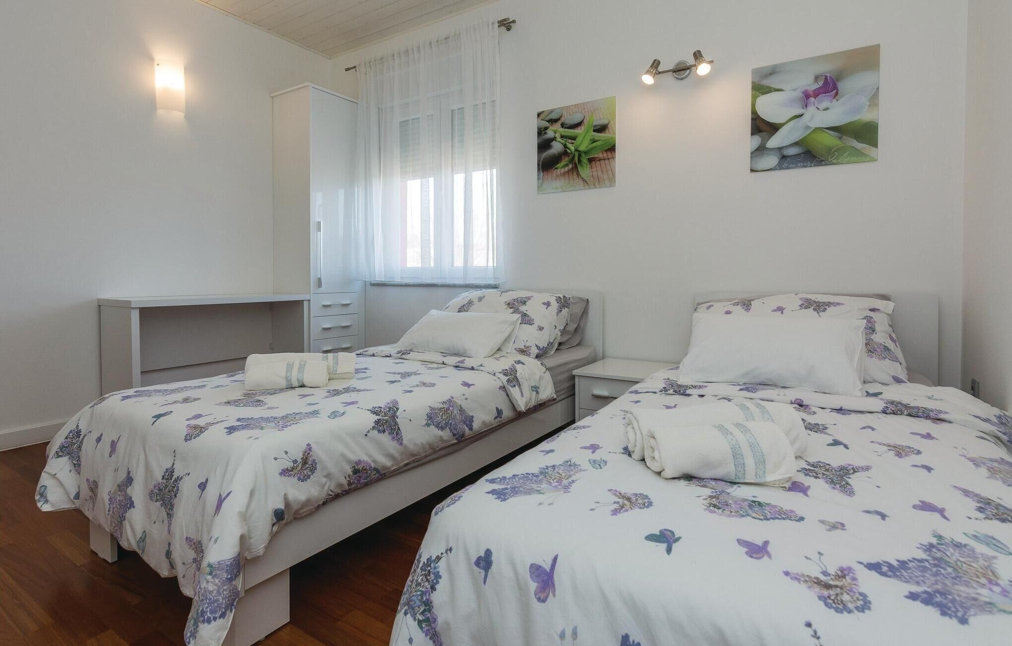Ein Schlafzimmer mit zwei Betten, einem Schreibtisch und einem Fenster mit durchsichtigen Vorhängen.