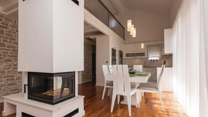 Een moderne woonkamer met een open haard, een eethoek met witte stoelen, en een keuken op de achtergrond.