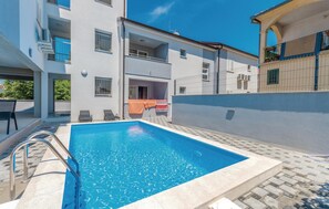 Una piscina con una escalera metálica, rodeada de una zona pavimentada con sillones de descanso.