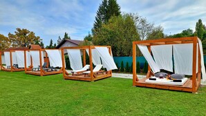 A row of wooden gazebos with white canopies, each with a lounge chair and a small table. - Gorgeous home in Fericanci with sauna (Fericanci)
