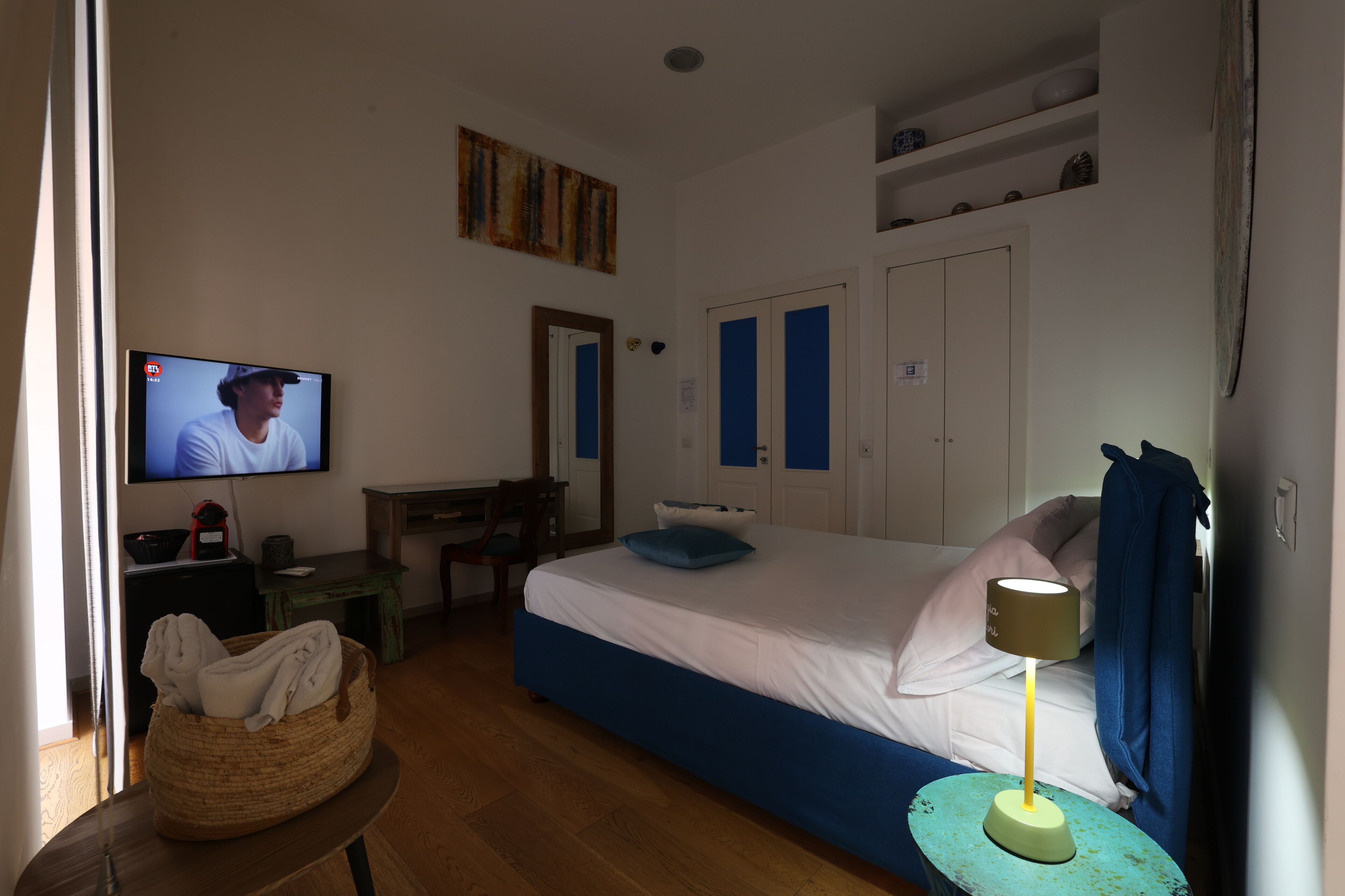Una camera d'albergo con un letto, una scrivania, una televisione e una lampada.