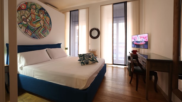 A bedroom with a bed, a desk, a television, and a large painting on the wall. - Dimora Megaride (Naples)