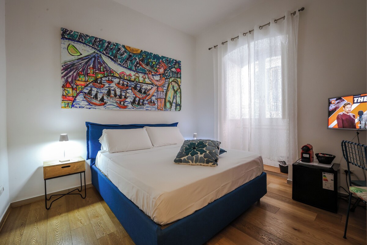 A bedroom with a bed, a nightstand, a TV, and a painting on the wall.