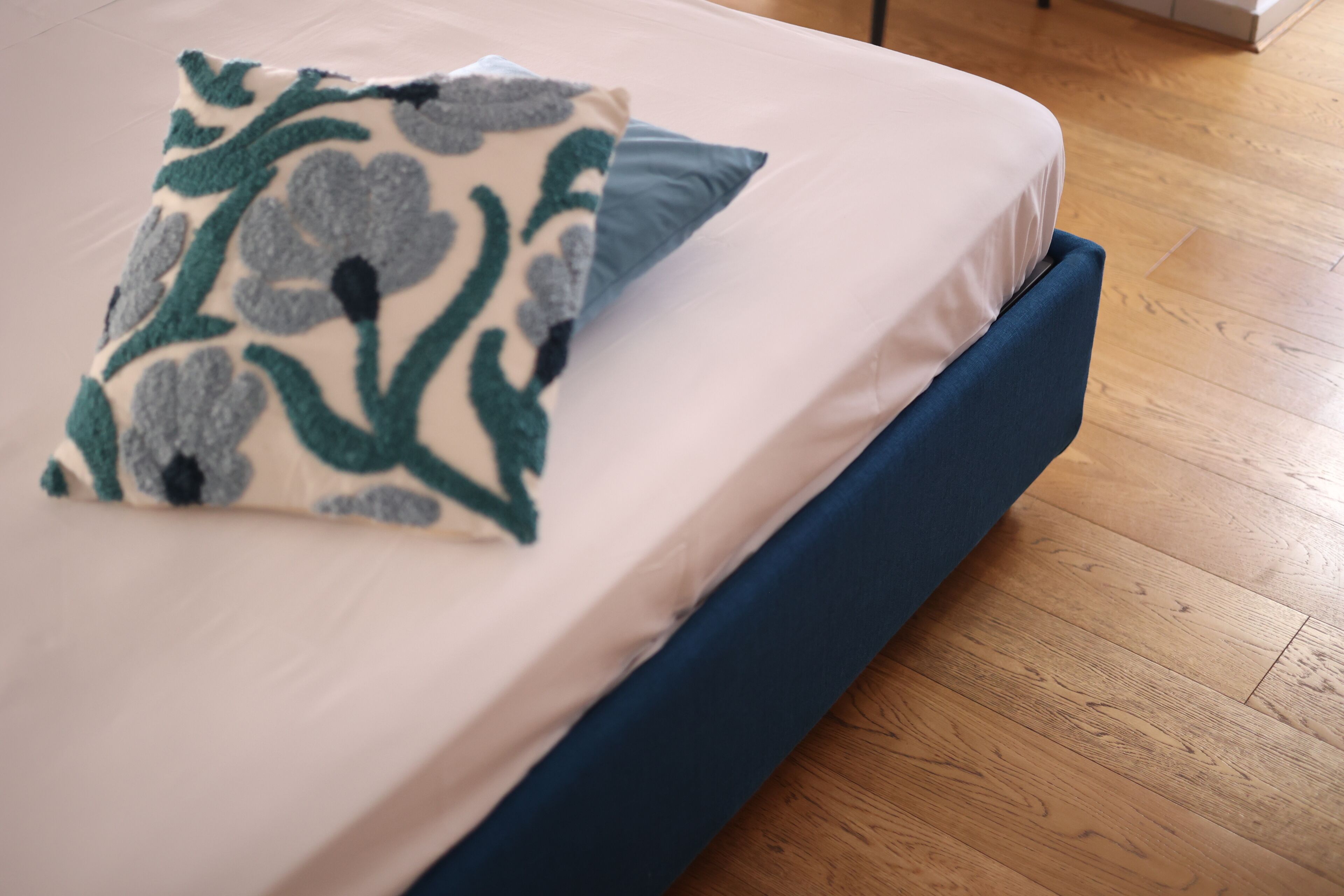Una cama con cabecera azul, colchón blanco y almohada estampada con motivos florales.