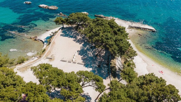 An aerial view of a beach with clear turquoise waters, rocky outcrops, and dense green pine trees. - Stunning home in Split (Split)