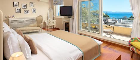 A hotel room with a large bed, a TV, a fireplace, and a balcony with a view of the sea.