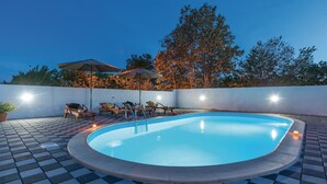 A swimming pool with lounge chairs and umbrellas, surrounded by a white wall and trees. - Lovely home in Pristeg (Pristeg)