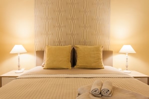 A neatly made bed with two pillows, a folded towel, and two bedside lamps. - Central Apartment near Metro station (Athens)