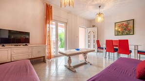 Una habitación de hotel con televisión, una mesa de comedor con sillas, cama y una araña.