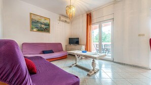 Una sala de estar con un sofá morado, un televisor sobre un mueble y una mesa con un tazón azul.