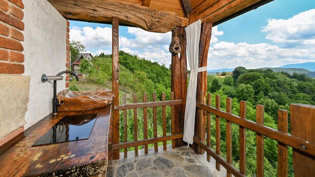 A rustic bathroom with a wooden sink, stone floor, and a view of a lush green landscape.