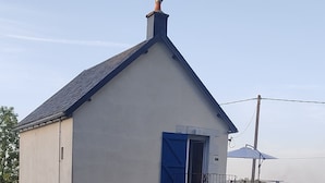 Un edificio a un piano con tetto spiovente, una porta blu e un camino.